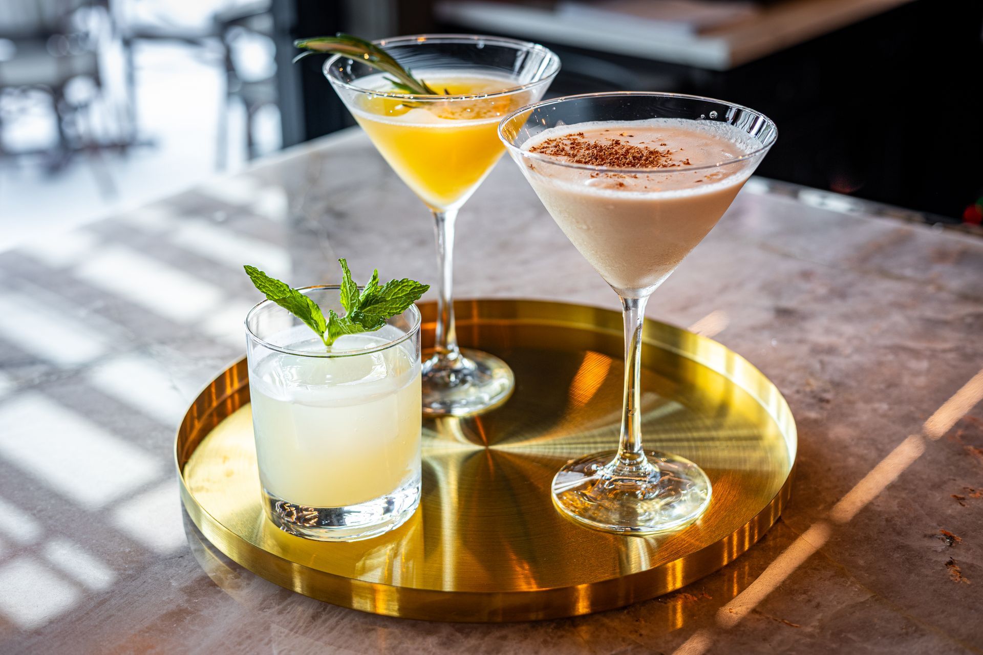 Three cocktails are sitting on a gold tray on a table.