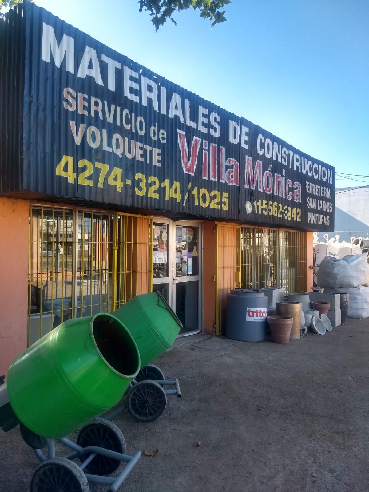 Una mezcladora de cemento verde está frente a un edificio que dice materiales de construcción