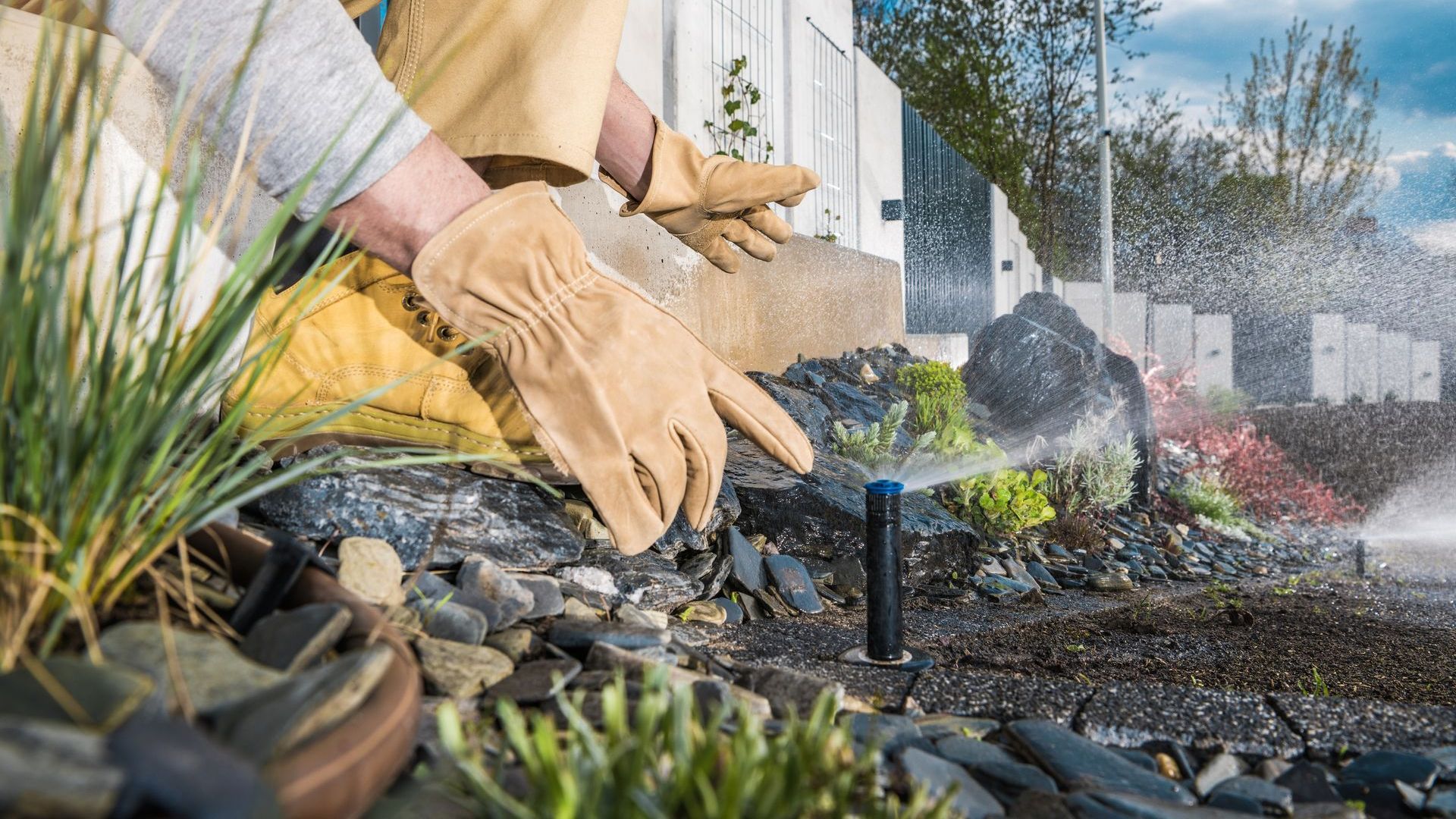 A person wearing gloves is working on a sprinkler in a garden.