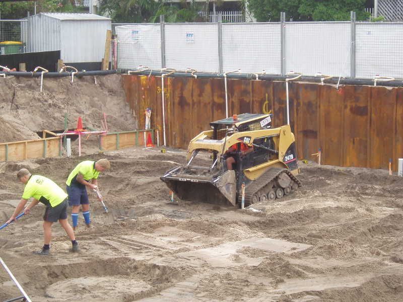 Construction workers smoothing muddy ground with a skid-steer loader at a work site
