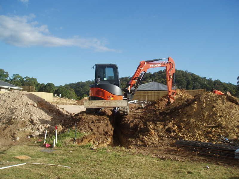 Two excavators digging a trench beside large dirt piles on a grassy construction site