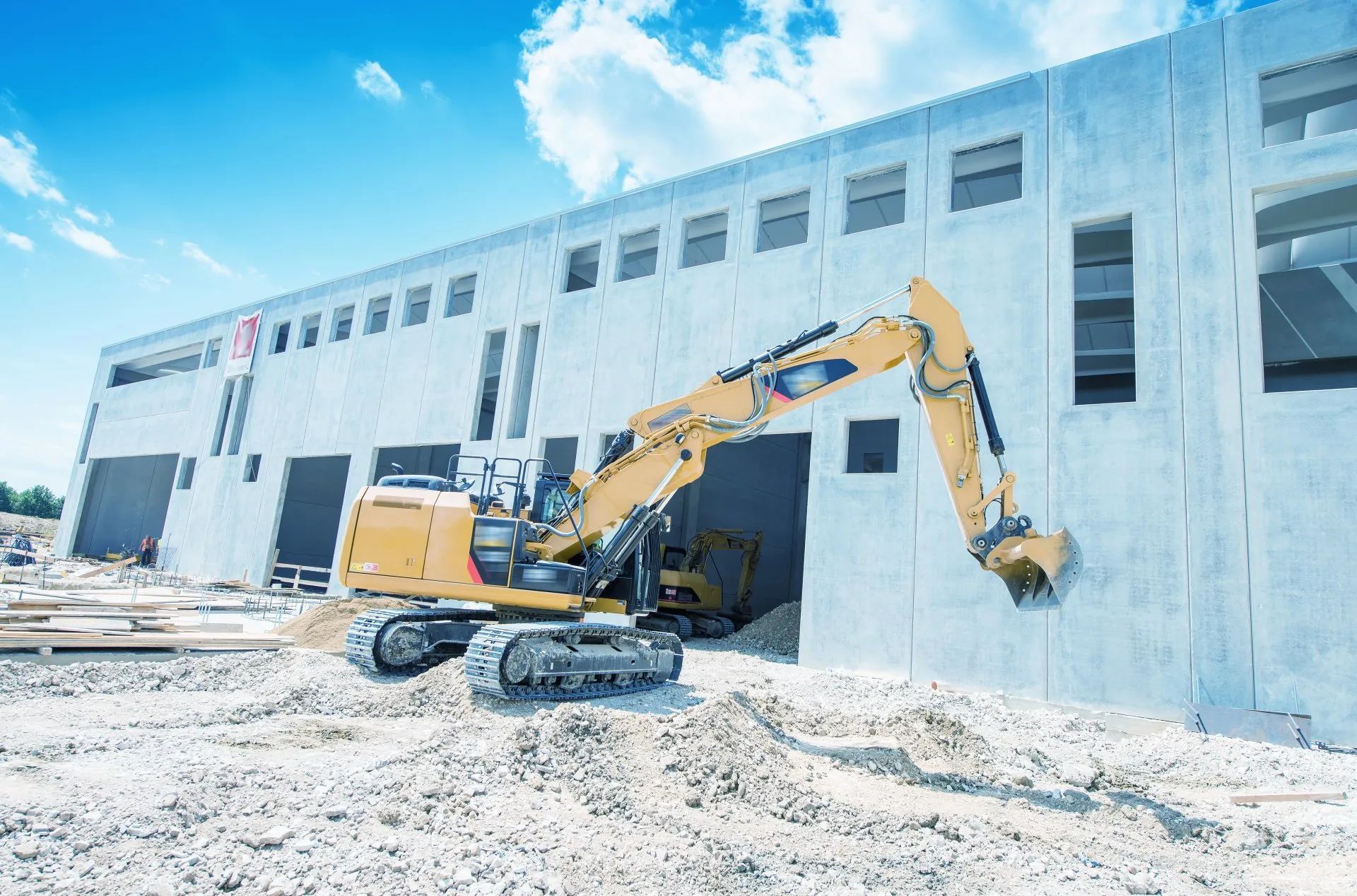 Yellow excavator demolishing a white industrial building under a bright blue sky