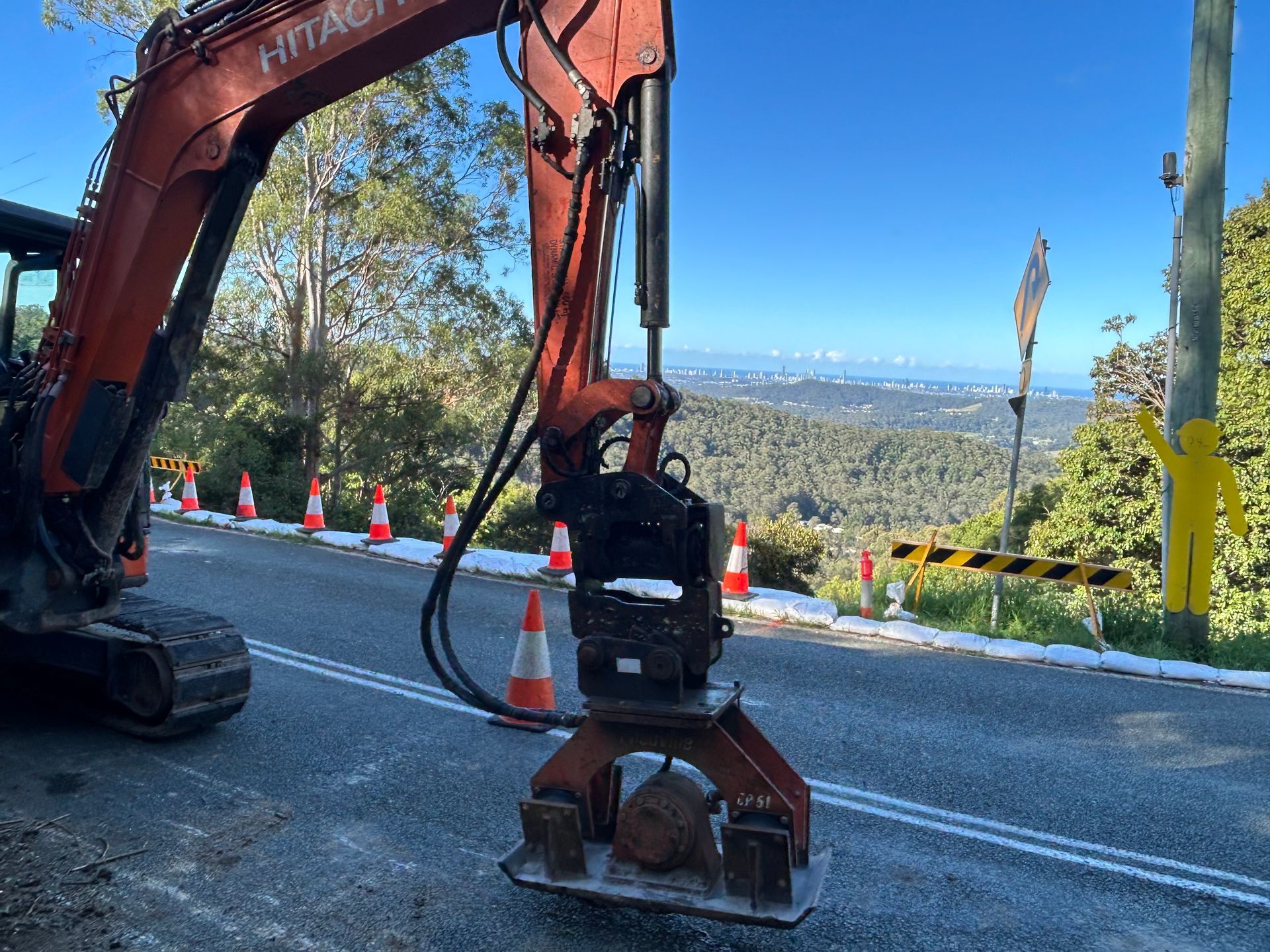 Excavator fitting roadside guardrail posts with mountain view in the background