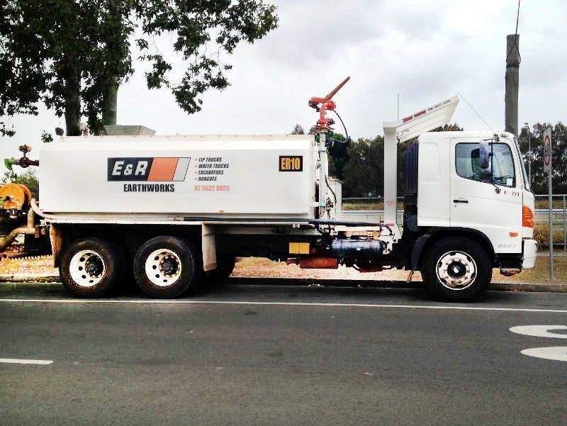 White E&R sanitation truck parked on a street beside trees and a curb