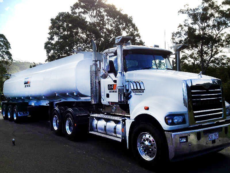 White tanker truck parked on a road with trees in the background