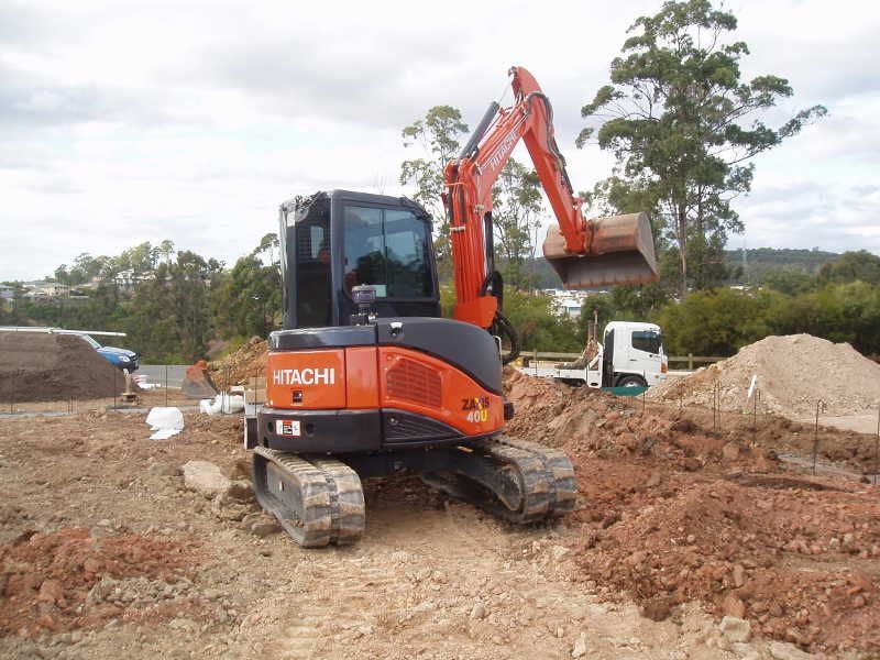 Orange Hitachi excavator on a muddy construction site with dirt piles and trees in the background