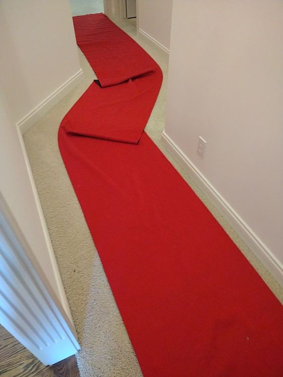 Red carpet runner laid down a narrow hallway, bending around a corner.