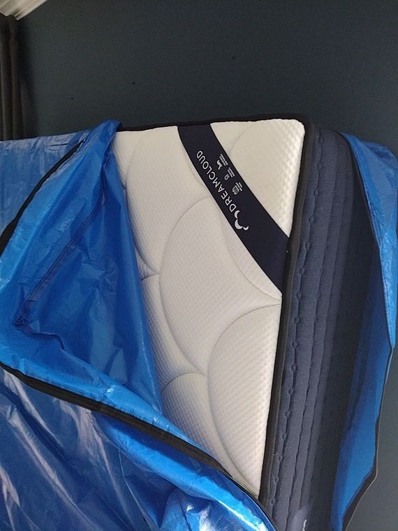 Blue tarp partially covering a mattress with a white quilted surface and dark navy border.