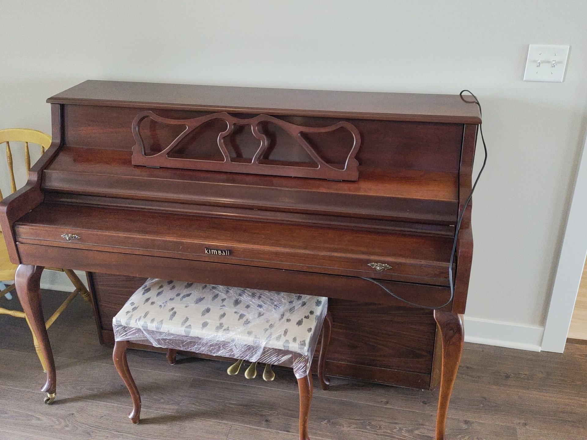 Wooden upright piano against a wall with a bench in front of it
