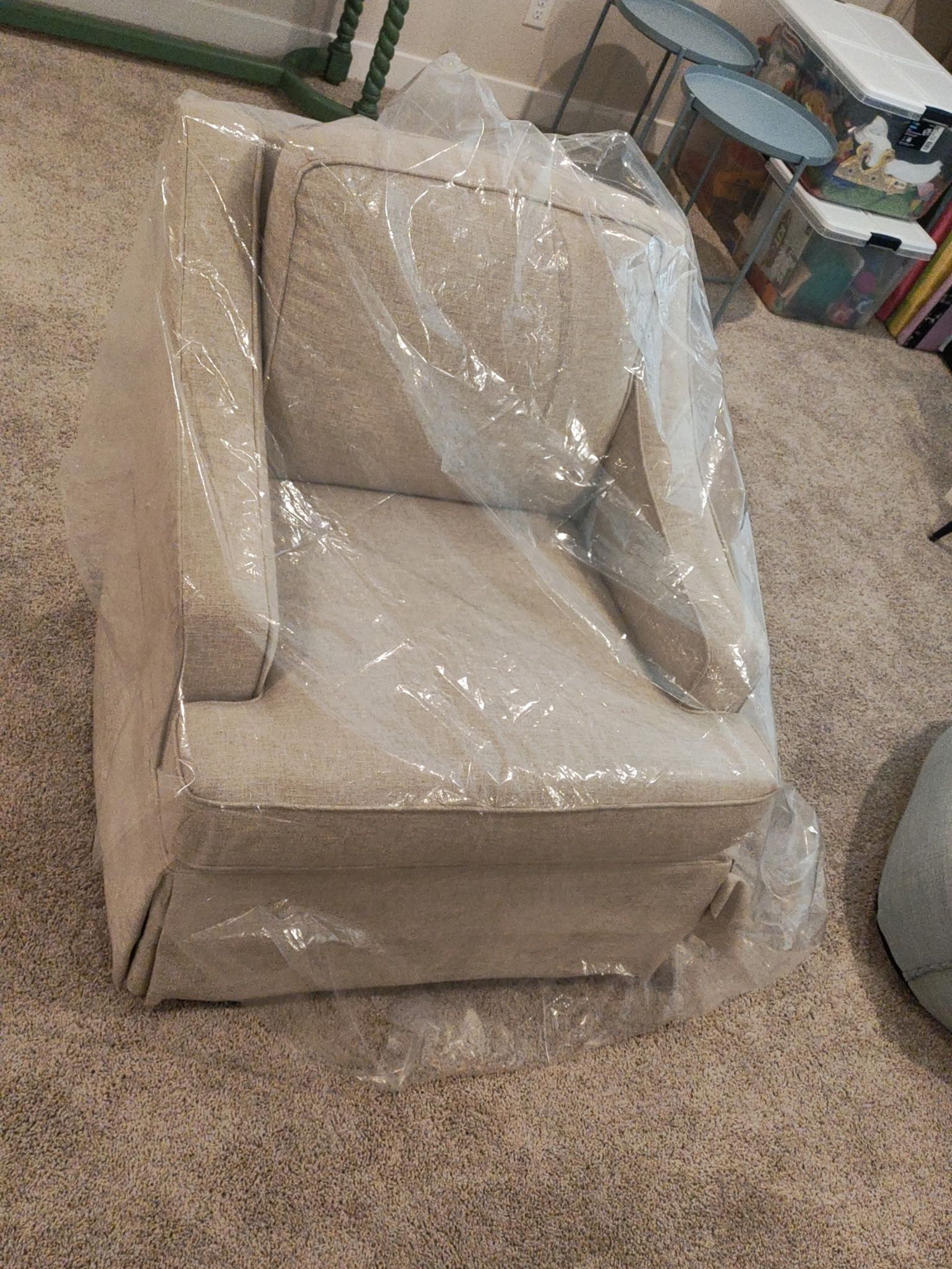 Beige armchair wrapped in clear plastic in a room with carpeted floor.