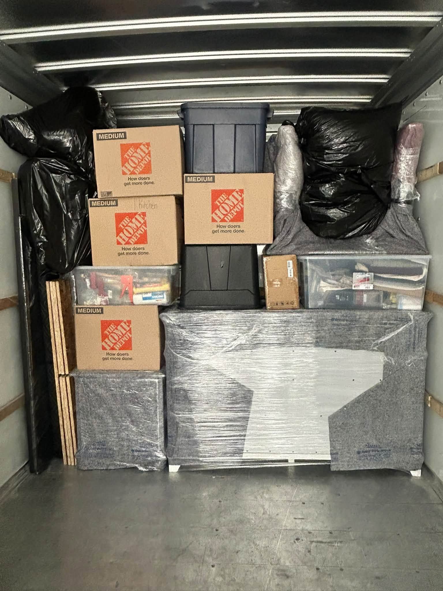 Packed moving truck with stacked boxes, wrapped furniture, and bags secured inside.
