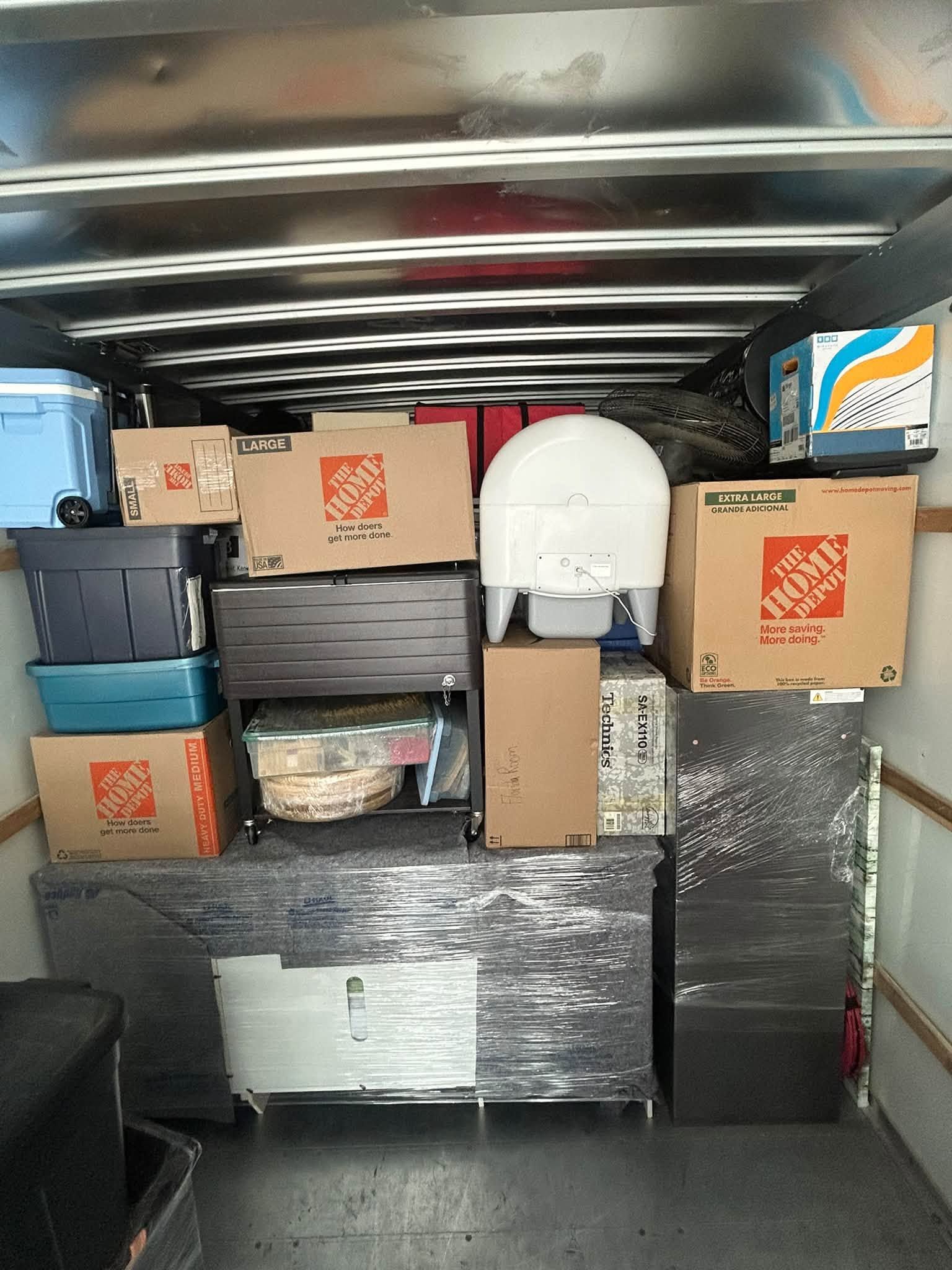 Packed moving truck loaded with stacked boxes, bins, and wrapped furniture in the cargo area