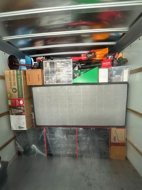 Inside a truck trailer, furniture and boxes are tightly stacked and secured for moving.