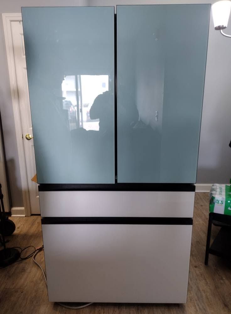 Blue-gray cabinet with two tall doors and a white lower section in a room, with a door and lamp beside it