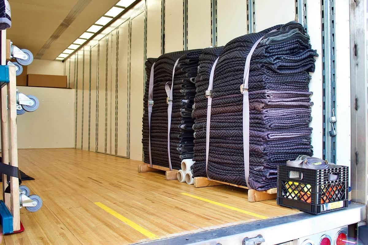 Stacked dark folded mats or blankets strapped on a pallet in a storage trailer with a wooden floor.
