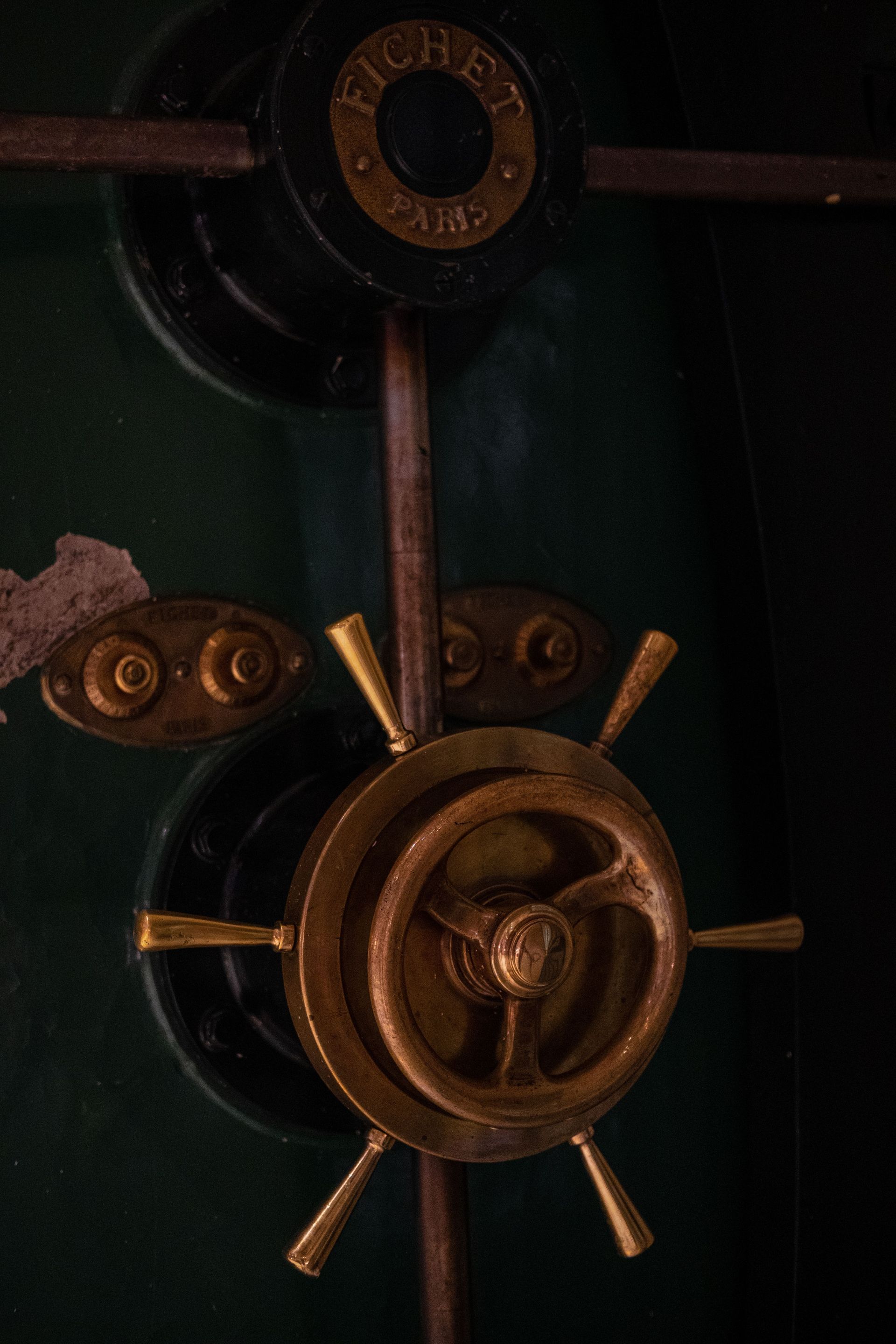 Dimly lit bronze safe lock with central wheel and metal spokes on a dark green door