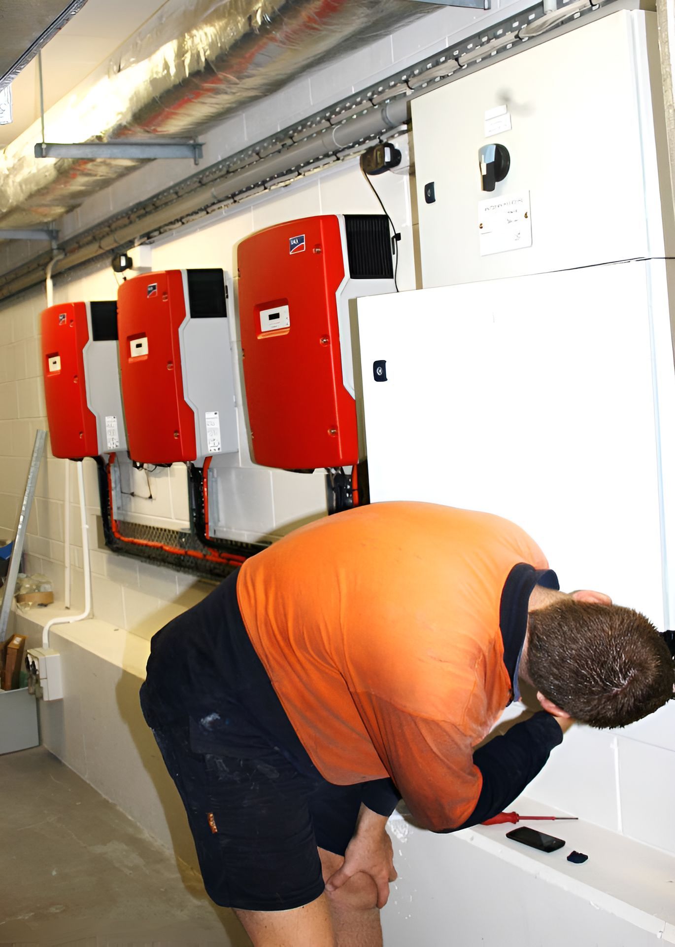 A Man In An Orange Shirt Is Working On A Solar Panel — Waltlec Industries In Garbutt, QLD