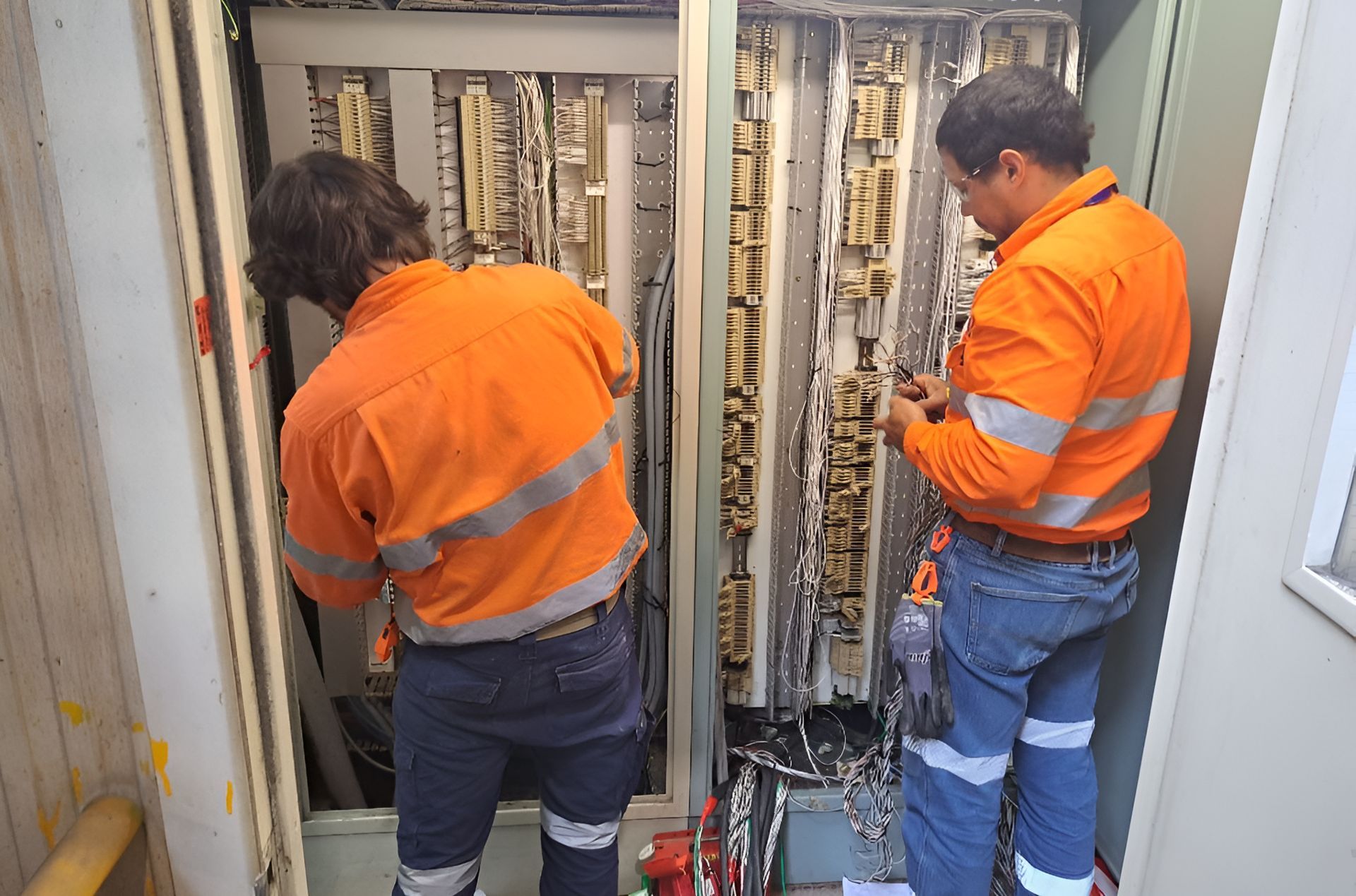 Two Men In Orange Shirts Are Working On A Electrical Box — Waltlec Industries In Garbutt, QLD