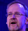 A man with glasses and a beard is speaking into a microphone.