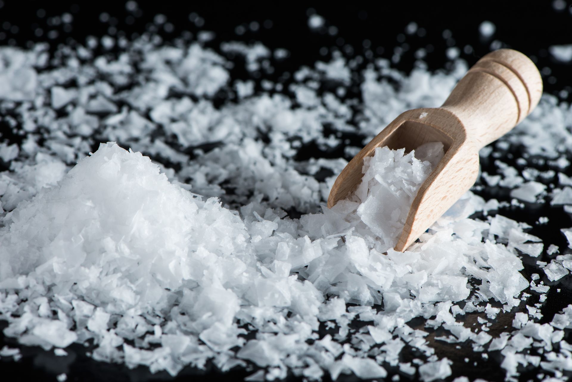 A wooden scoop filled with salt is sitting on top of a pile of salt.