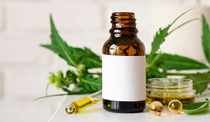 Amber bottle with white label, dropper, and jar of green herbs on a white table