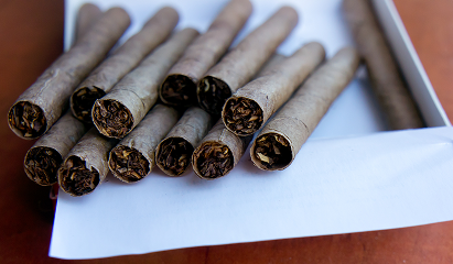 Several unlit cigarettes with brown filters and ash-filled tips on a white surface