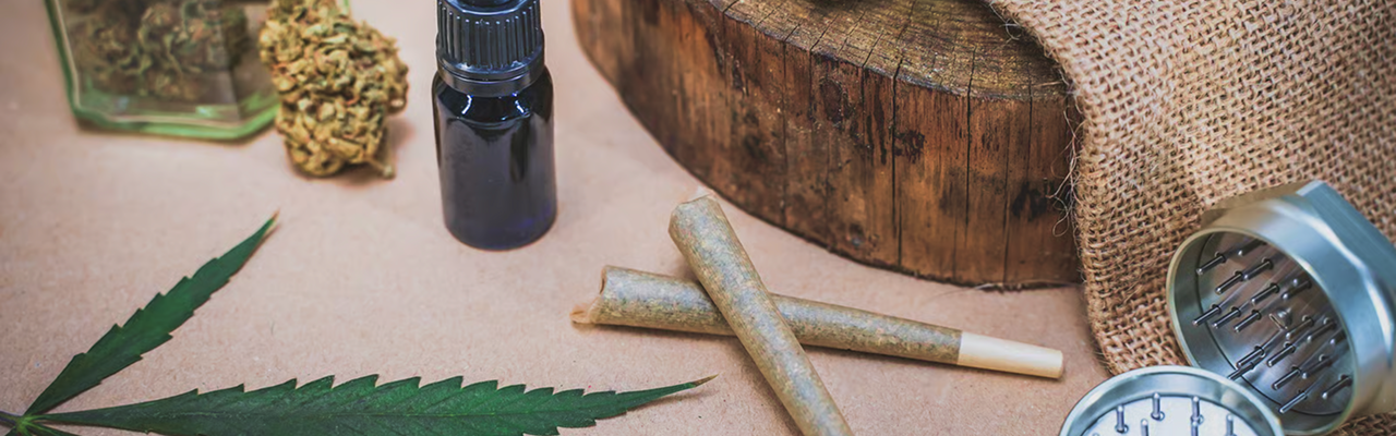 Cannabis buds, rolling papers, grinder, and green leaves on a wooden table