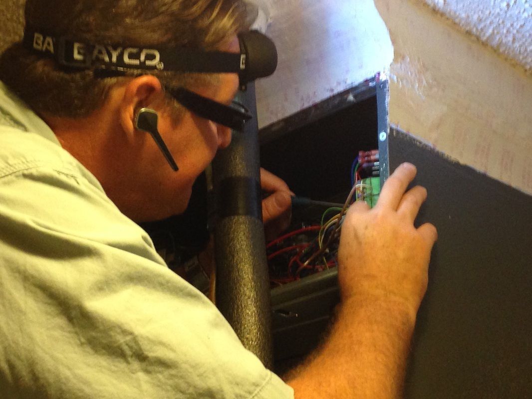 Man working on electrical wiring, wearing a headlamp. Inside a dark enclosure.