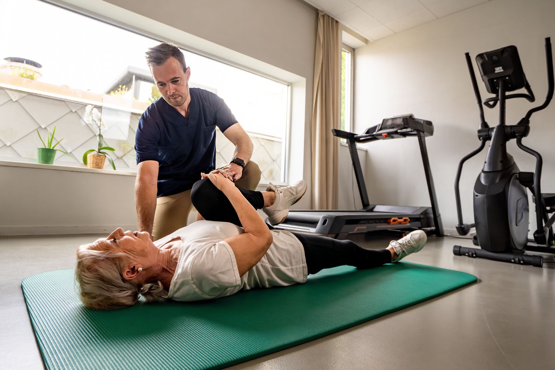 Physical therapist stretching a patient on a mat in a bright home gym. Physical therapist stretching a patient on a mat in a bright home gym.