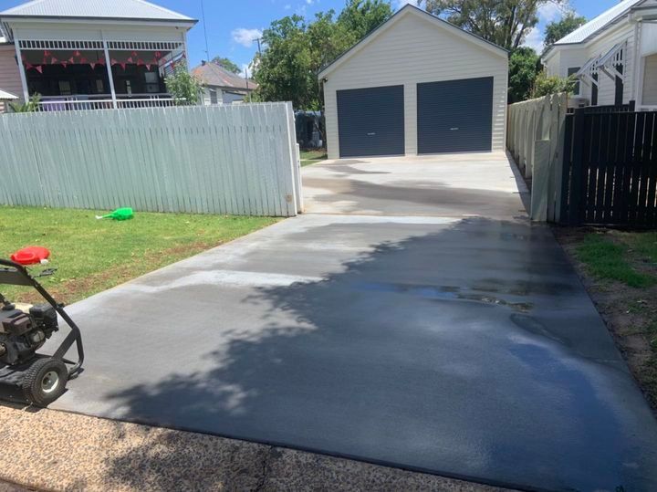 A Lawn Mower Is Sitting on A Concrete Driveway Next to A Garage — Pedro's Concreting in Warwick, QLD