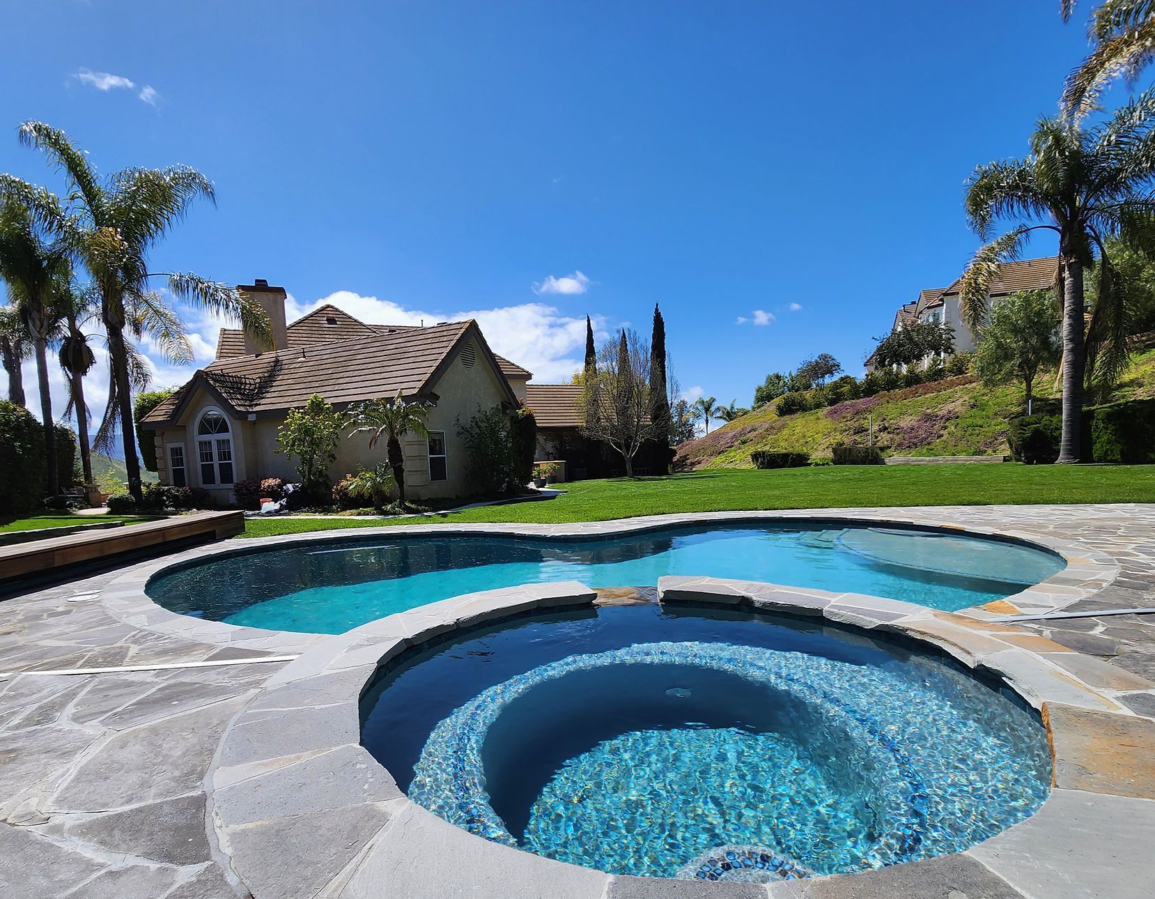 A large swimming pool with a hot tub in front of a house
