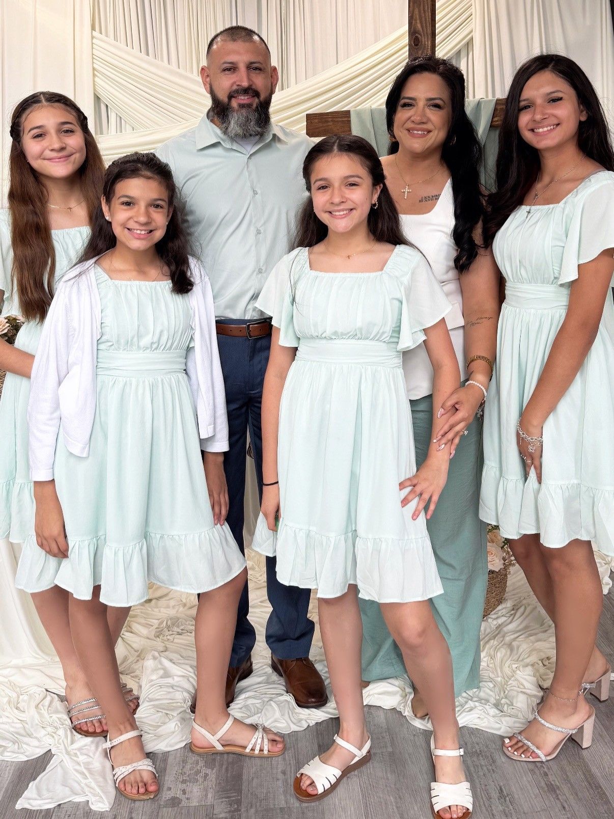 Family of six standing together indoors, wearing coordinated light blue and white outfits, smiling at the camera.