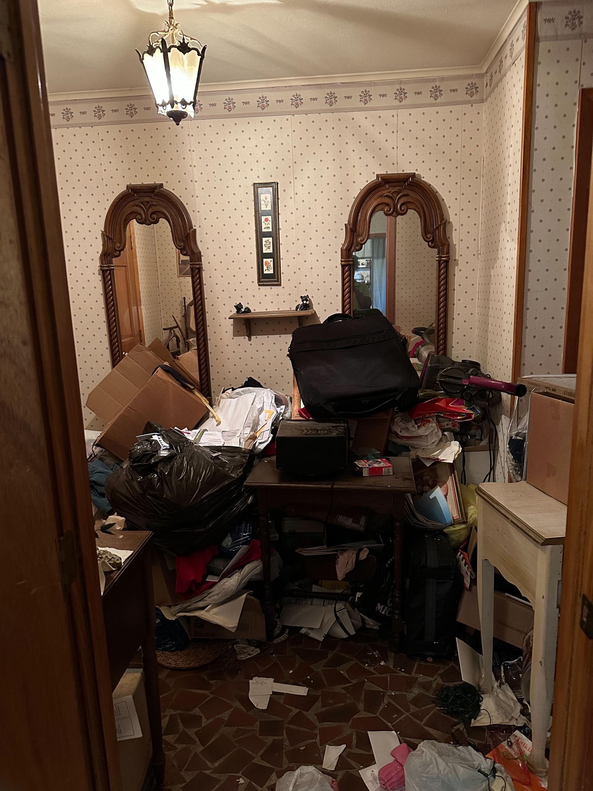 A messy room with two mirrors , a table , and a fireplace.