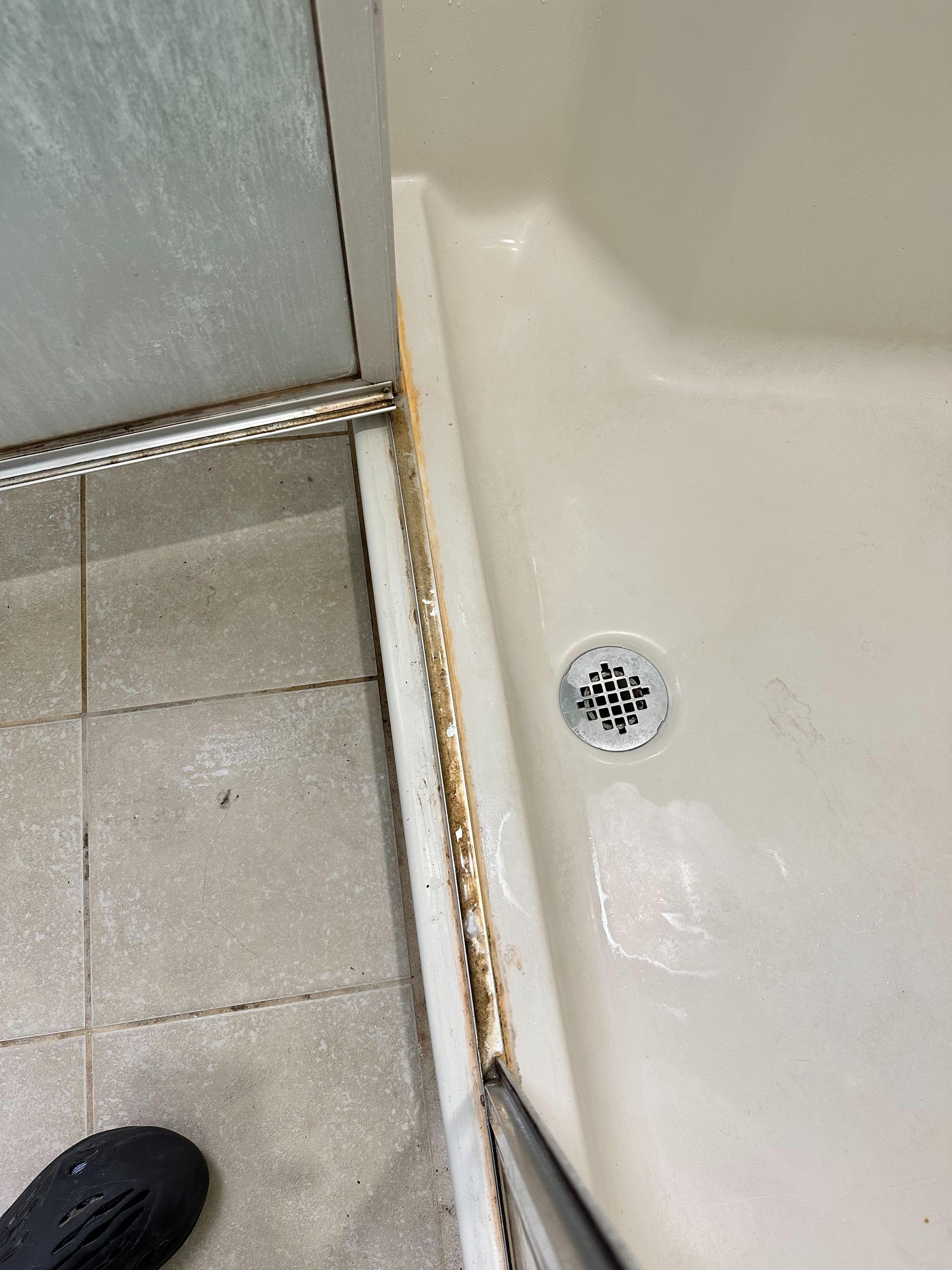 A person is standing next to a shower with a drain.