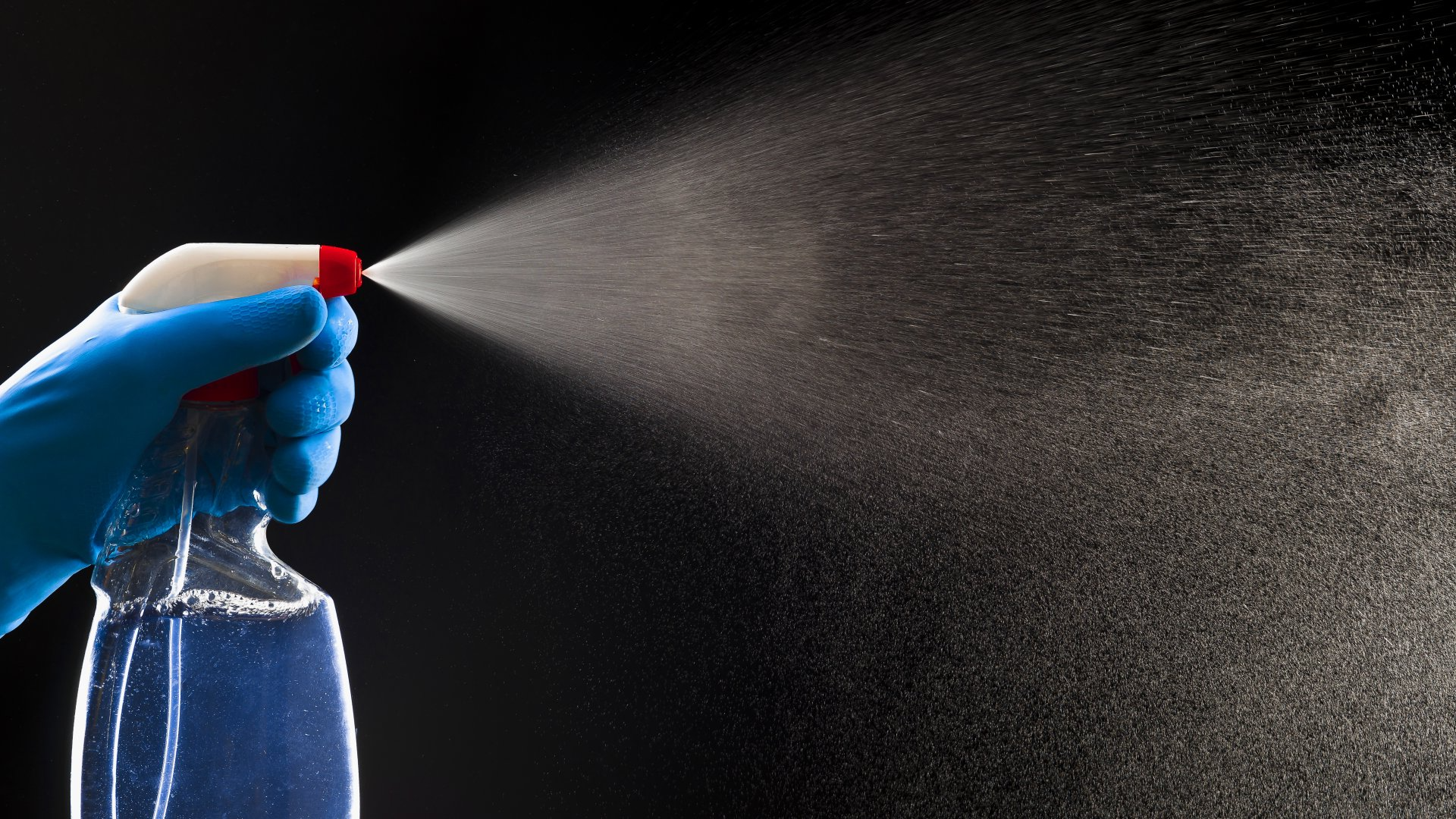 A person is spraying a bottle of cleaner on a black background.