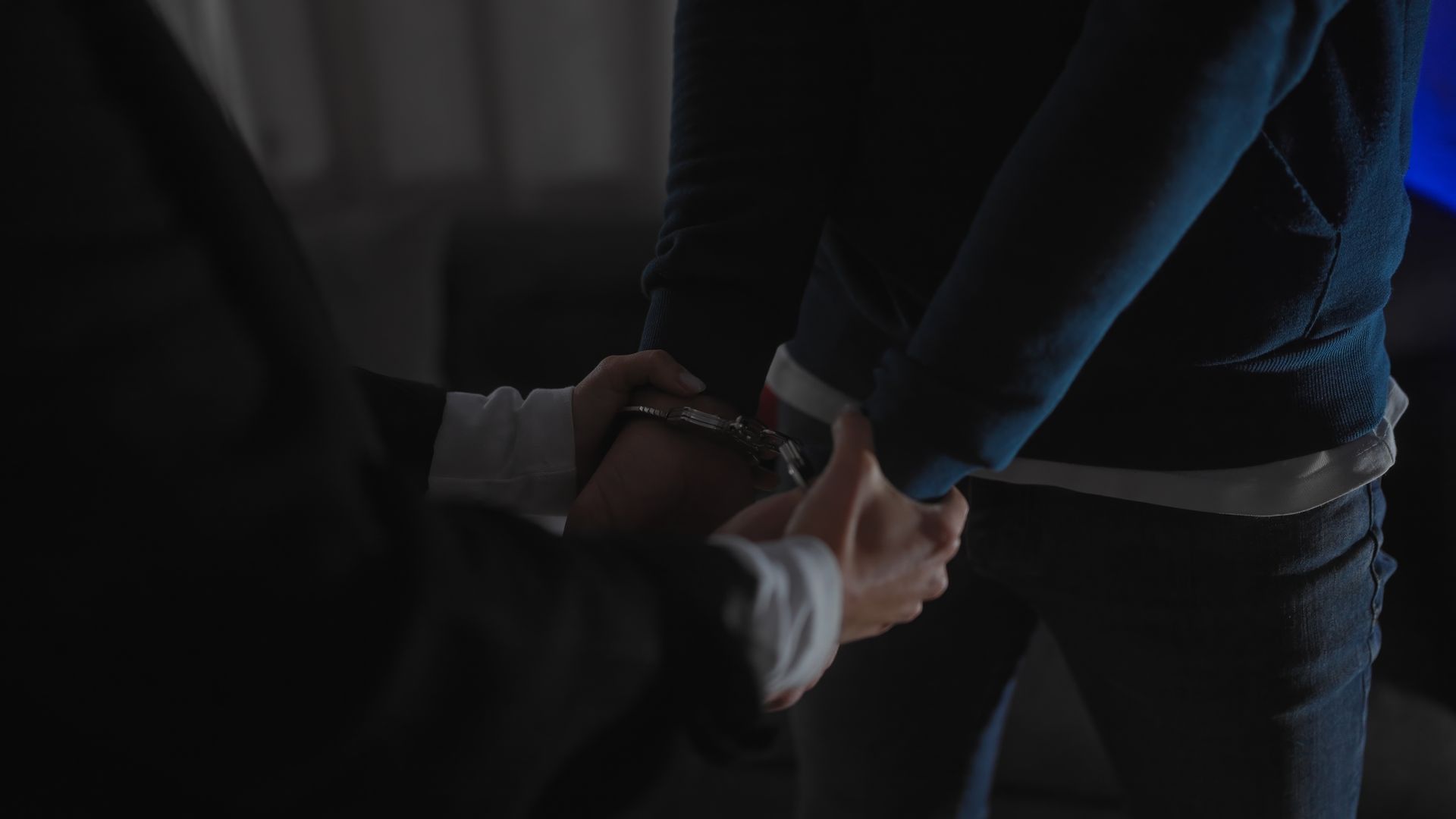 Person handcuffed by police in a dimly lit room