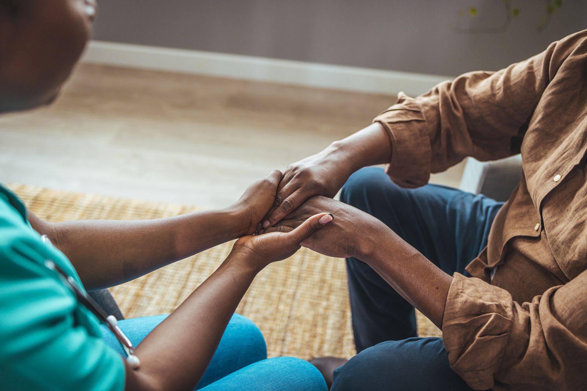 Two people sitting on a rug gently holding hands in a cozy room