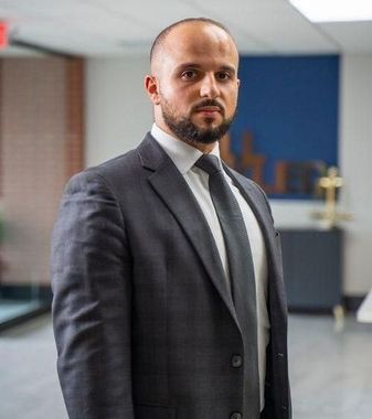 Man in a dark suit standing in a modern office hallway with a blurred background