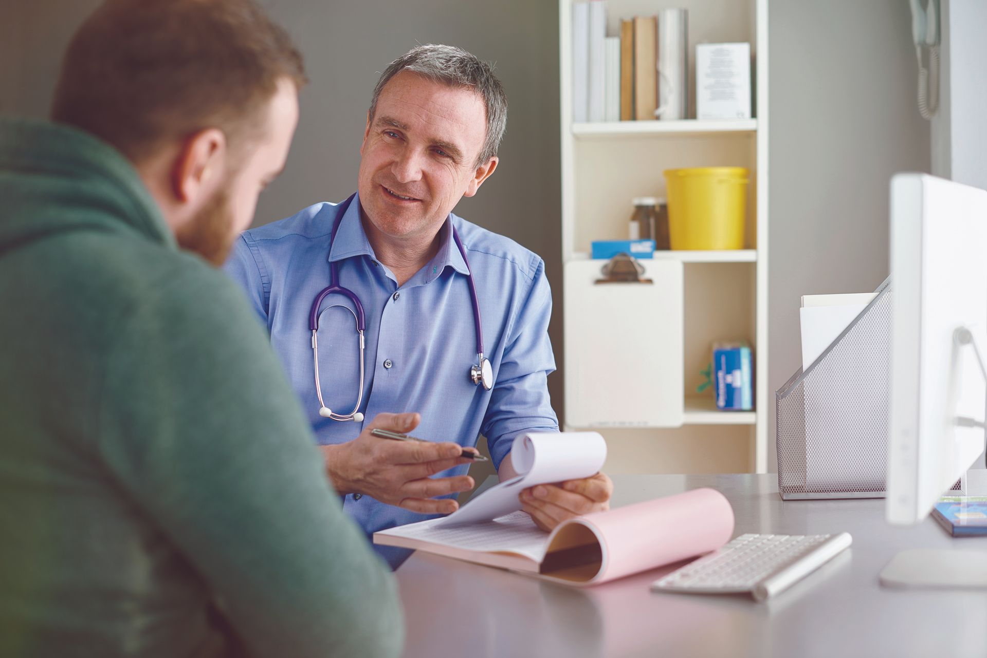 A man is sitting at a desk talking to a doctor.