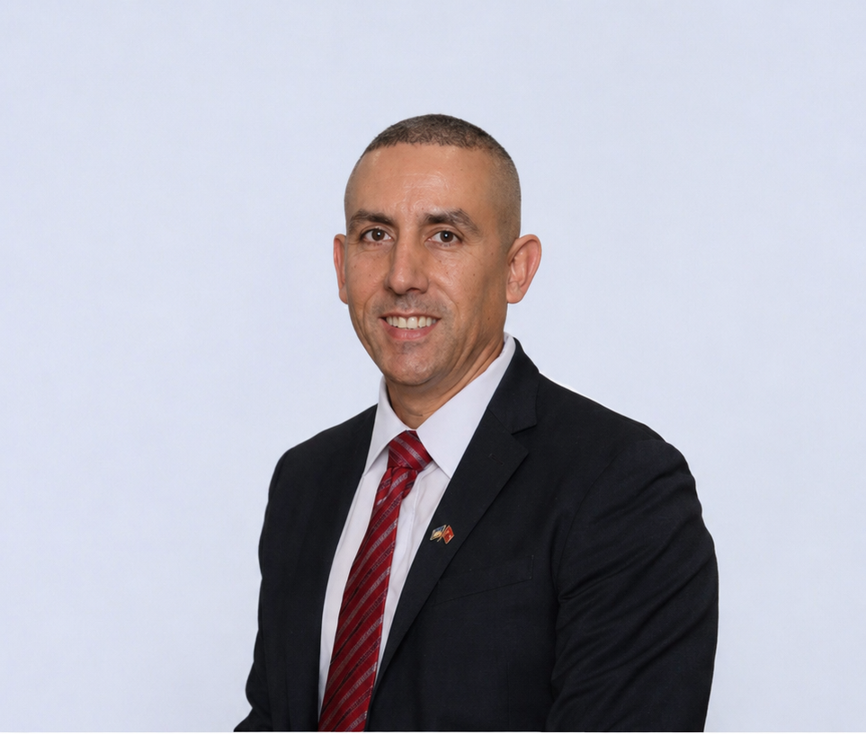 Man in a dark suit and red tie seated at a conference table in an office room.
