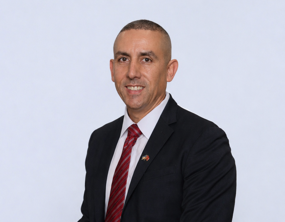 Man in a dark suit and red striped tie standing in a conference room, smiling at the camera