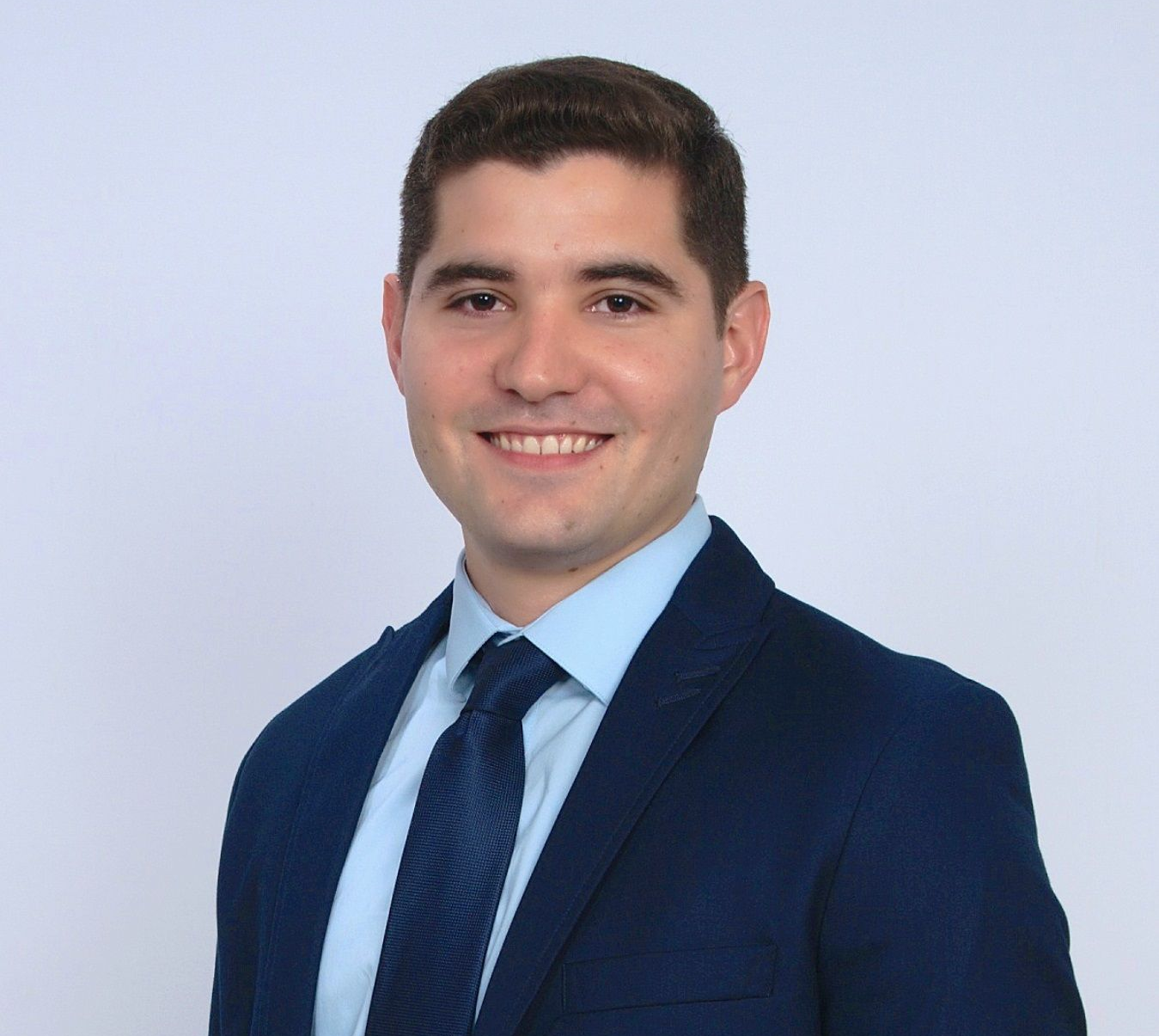 Smiling professional in a navy suit and blue tie against a light gray background