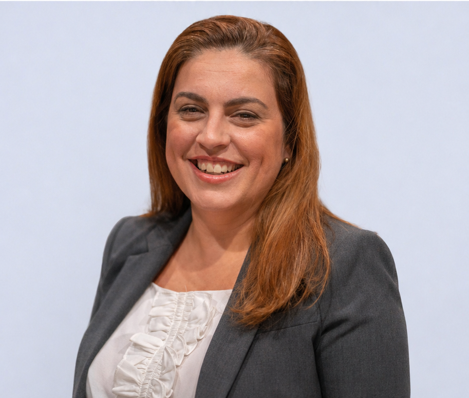 Smiling woman with long brown hair in a gray blazer against a blurred gray background
