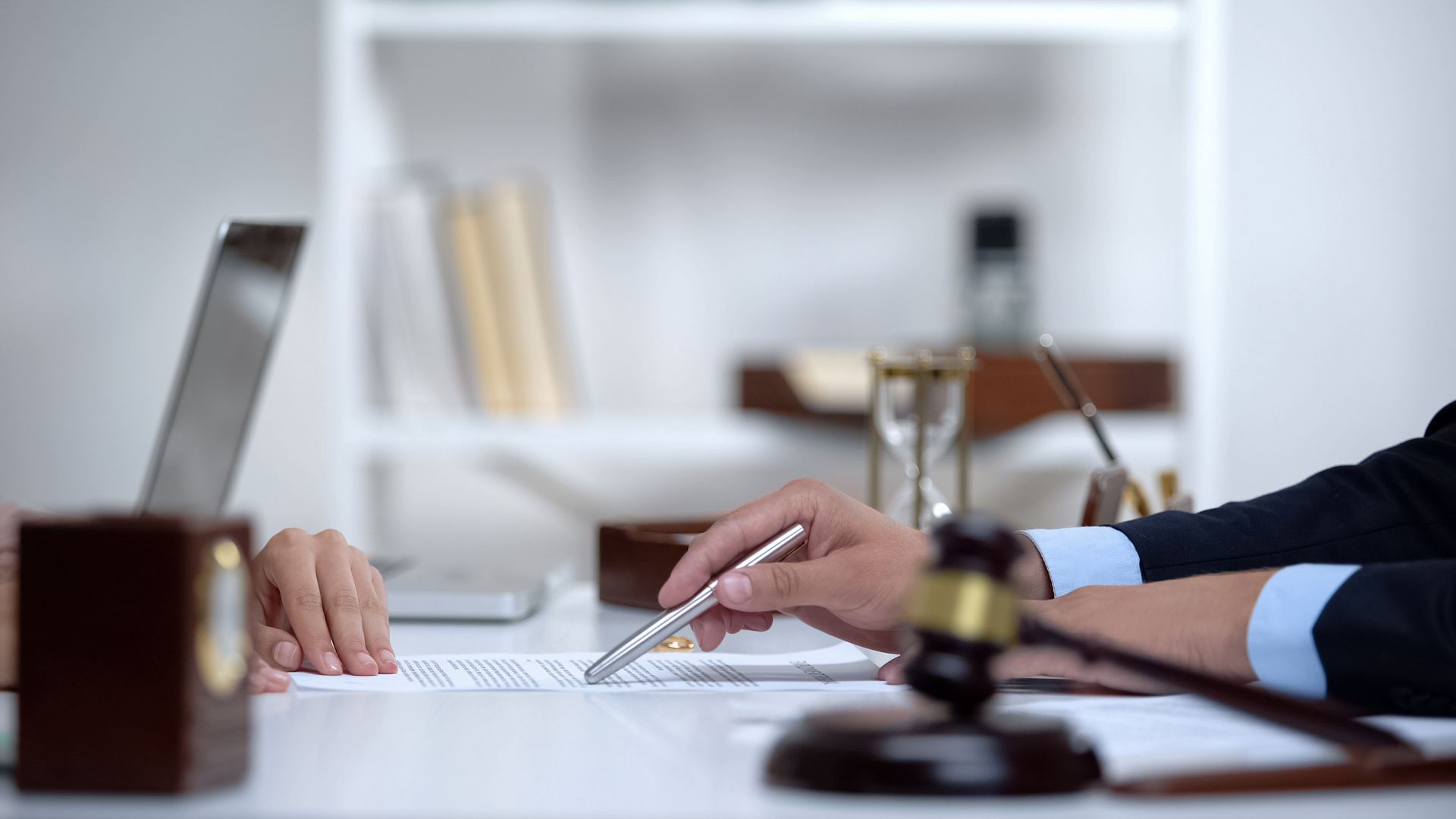 Hands signing a document on a desk with a judge’s gavel and laptop in the foreground