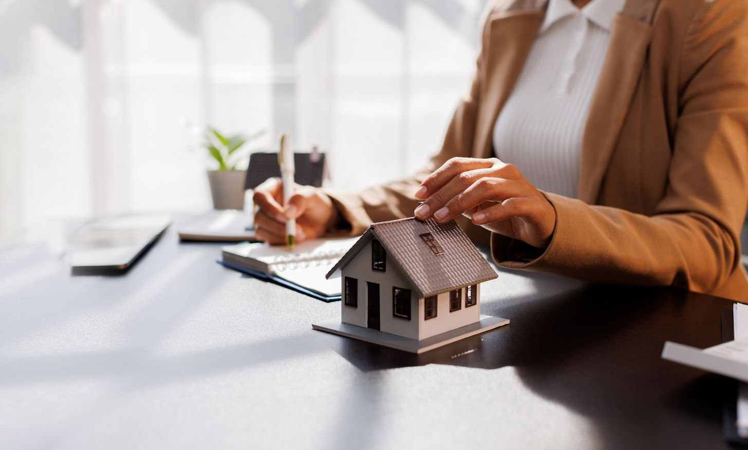 Person reviewing a small house model beside paperwork at a desk, suggesting a real estate meeting