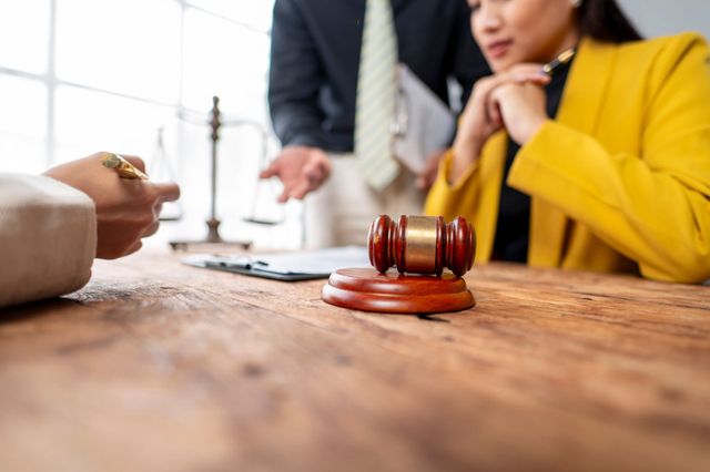 Gavel on a wooden table during a legal consultation, with two people discussing in the background