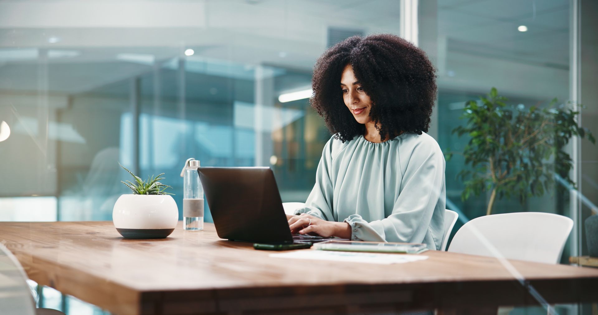 Woman working on a laptop at a wooden table in a bright modern office