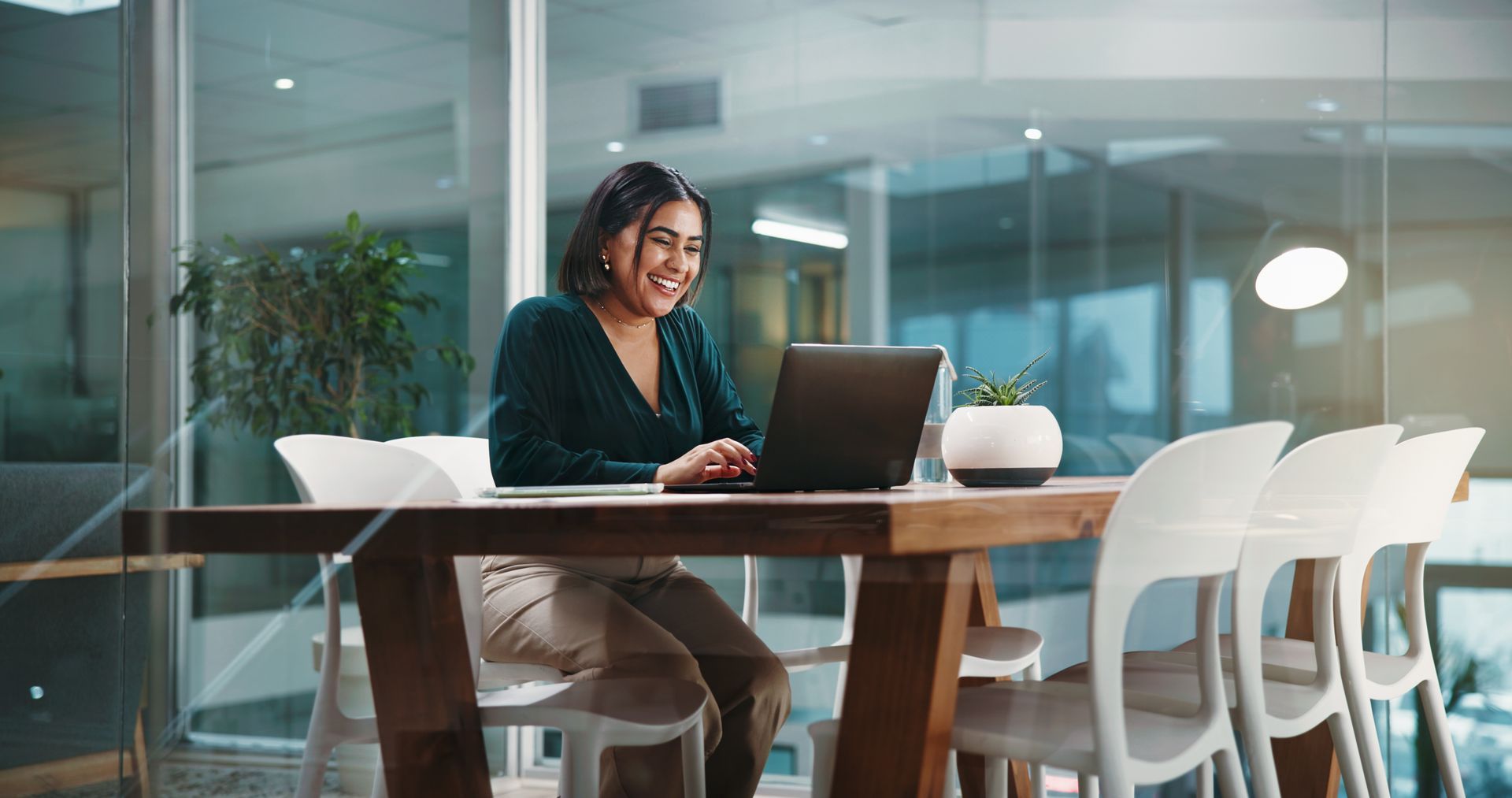 Person working on a laptop at a glass conference table in a modern office meeting room.
