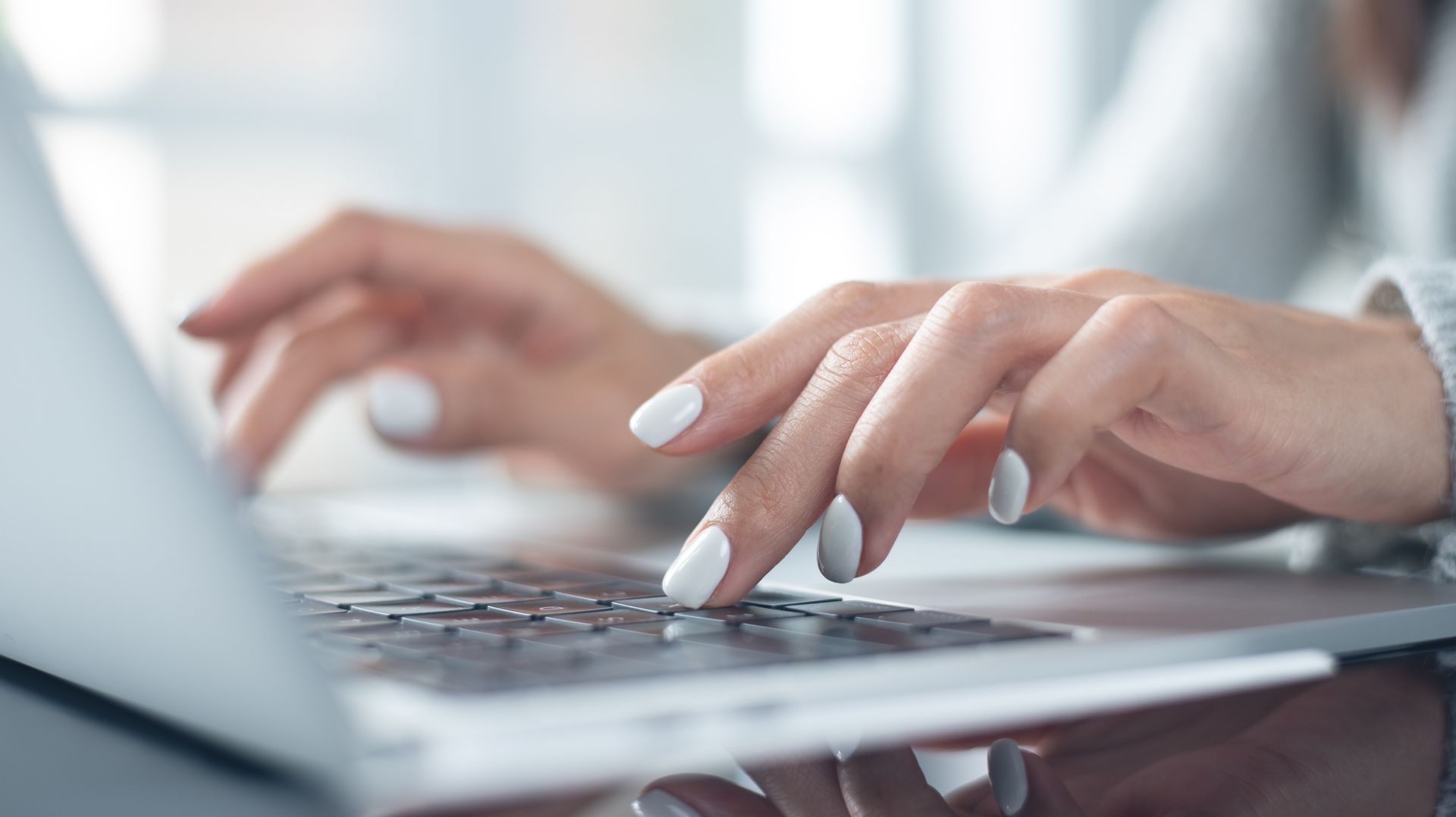 Hands typing on a laptop keyboard in a bright office setting