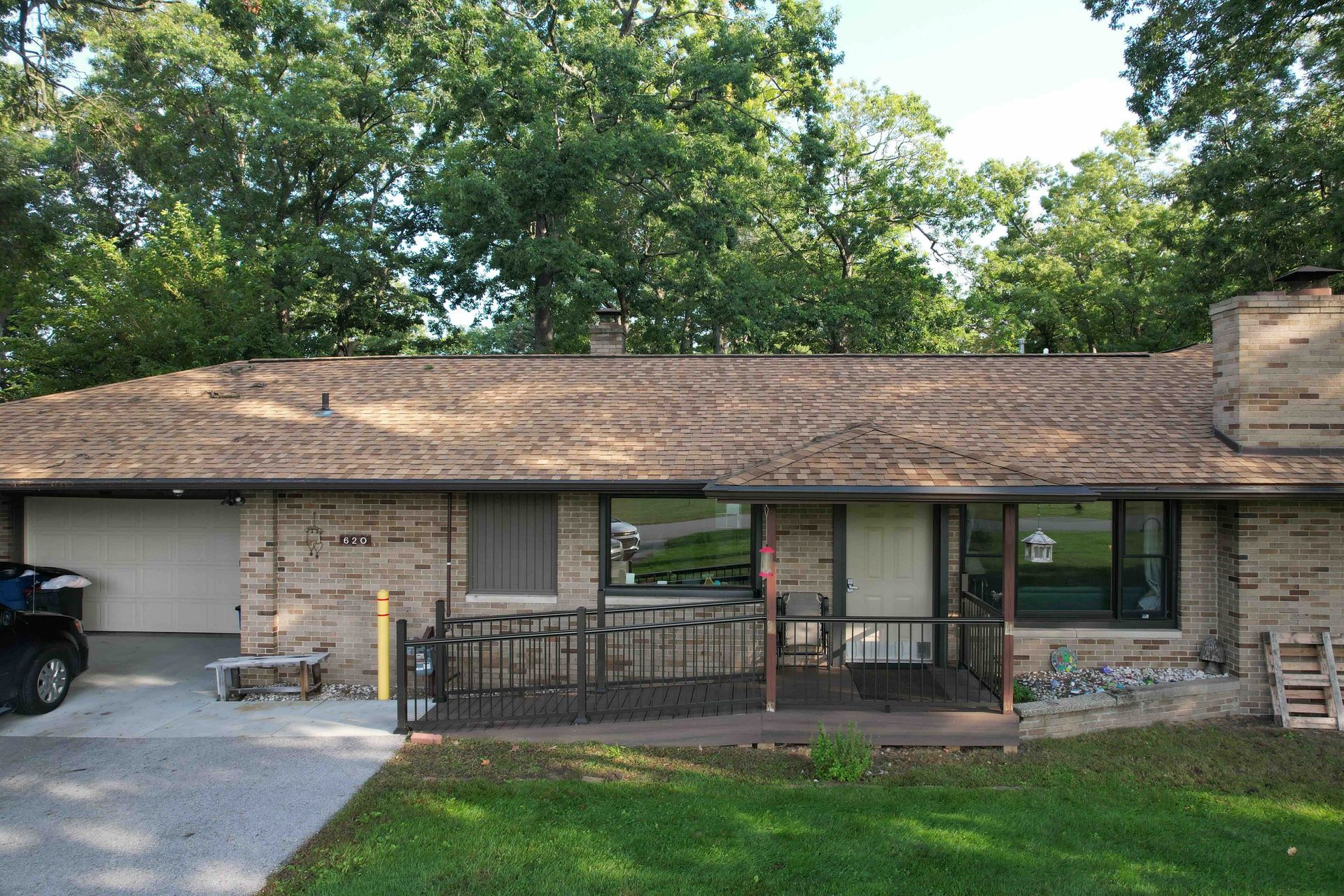 Single-story brick house with covered porch, windows, and a carport under trees
